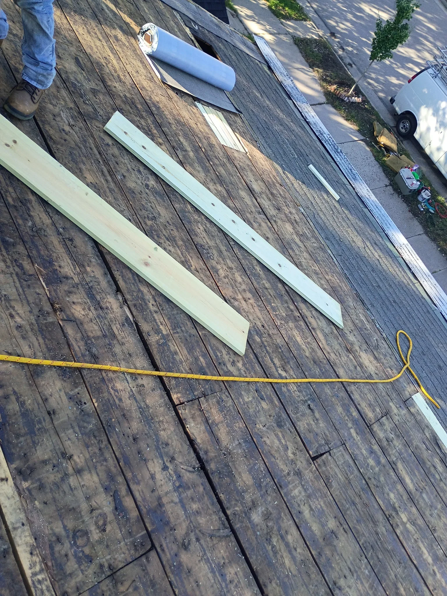 Exposed wood plank roof deck with new lumber boards, gray underlayment roll, and yellow chalk line during roof repair