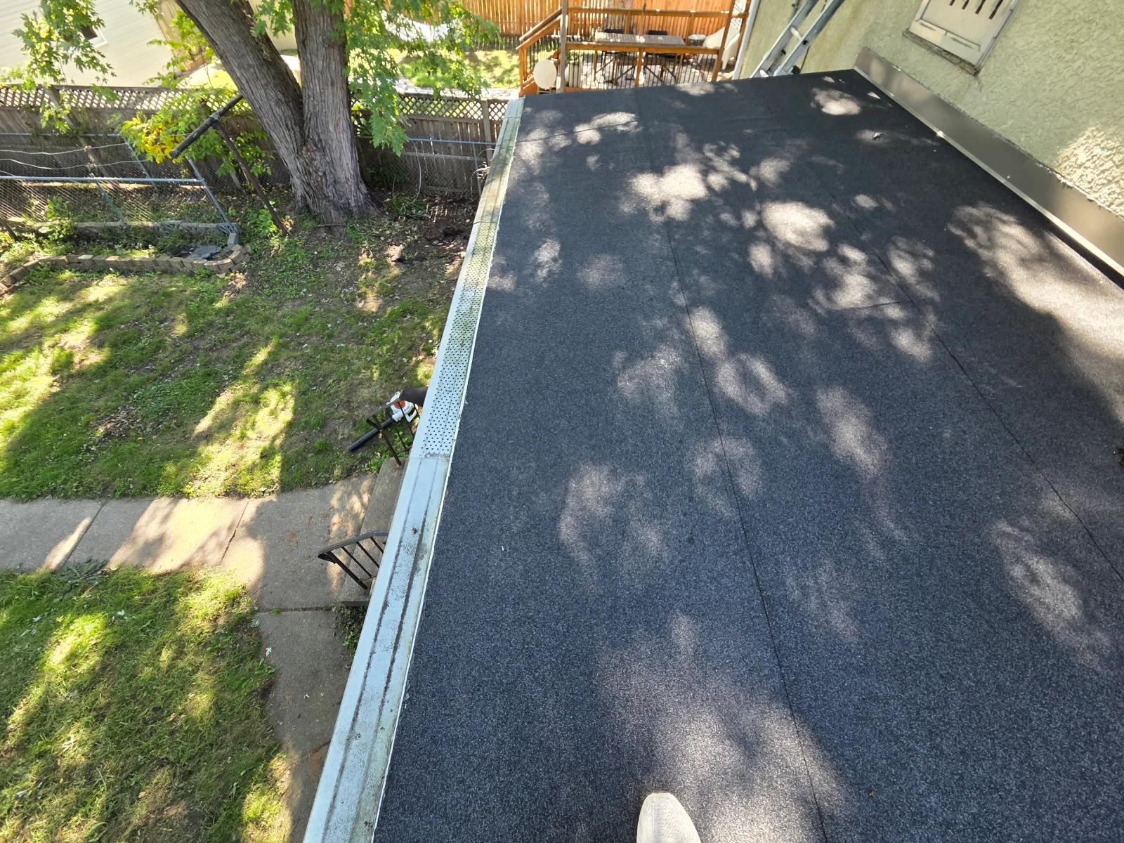 Dark granular flat roof membrane with seams and perforated metal drip edge flashing along the perimeter
