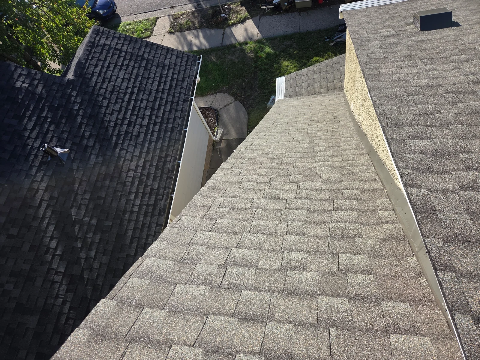 Aerial view of asphalt shingle roof with light gray and charcoal shingles, white metal gutter and drip edge, and roof vent.