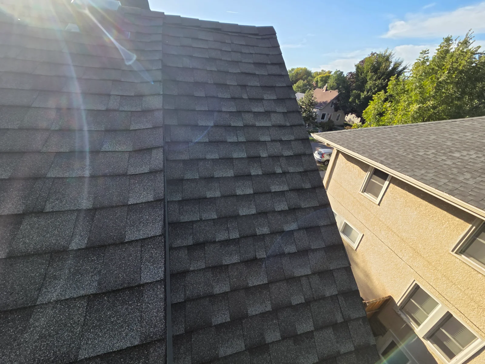 Dark gray architectural asphalt shingle roof with a center valley, next to a tan stucco building