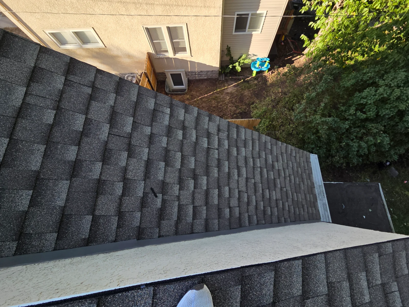 Dark charcoal architectural asphalt shingle roof with metal flashing and stucco-finished wall edge