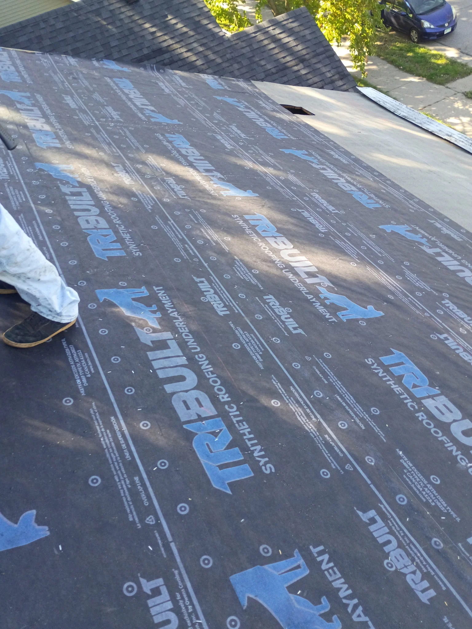 Installed TriBuilt synthetic roofing underlayment on a sloped roof deck with overlap lines and fastener marks visible