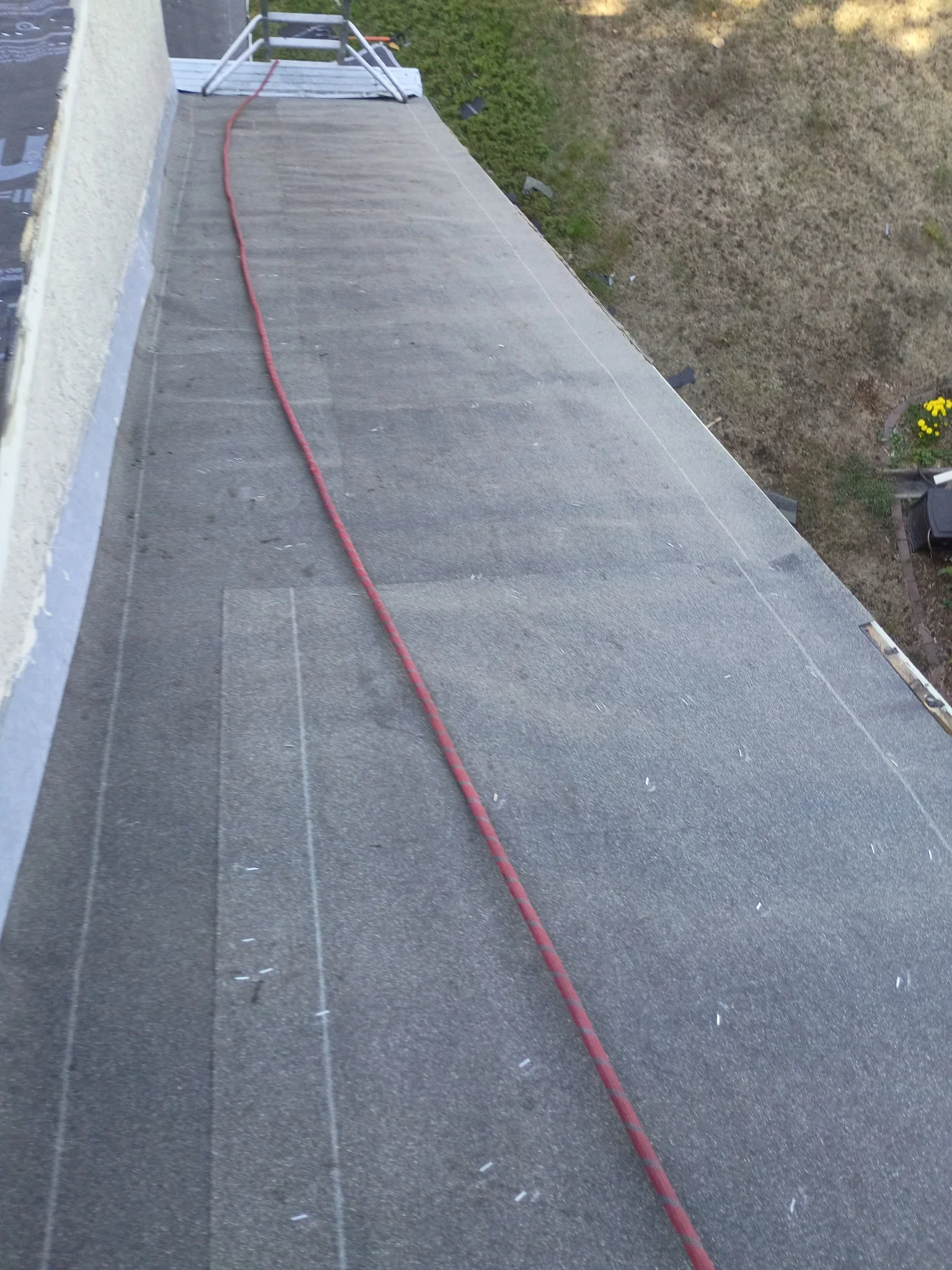 Low-slope roof with dark gray granular membrane, chalk layout lines, and red chalk line during installation