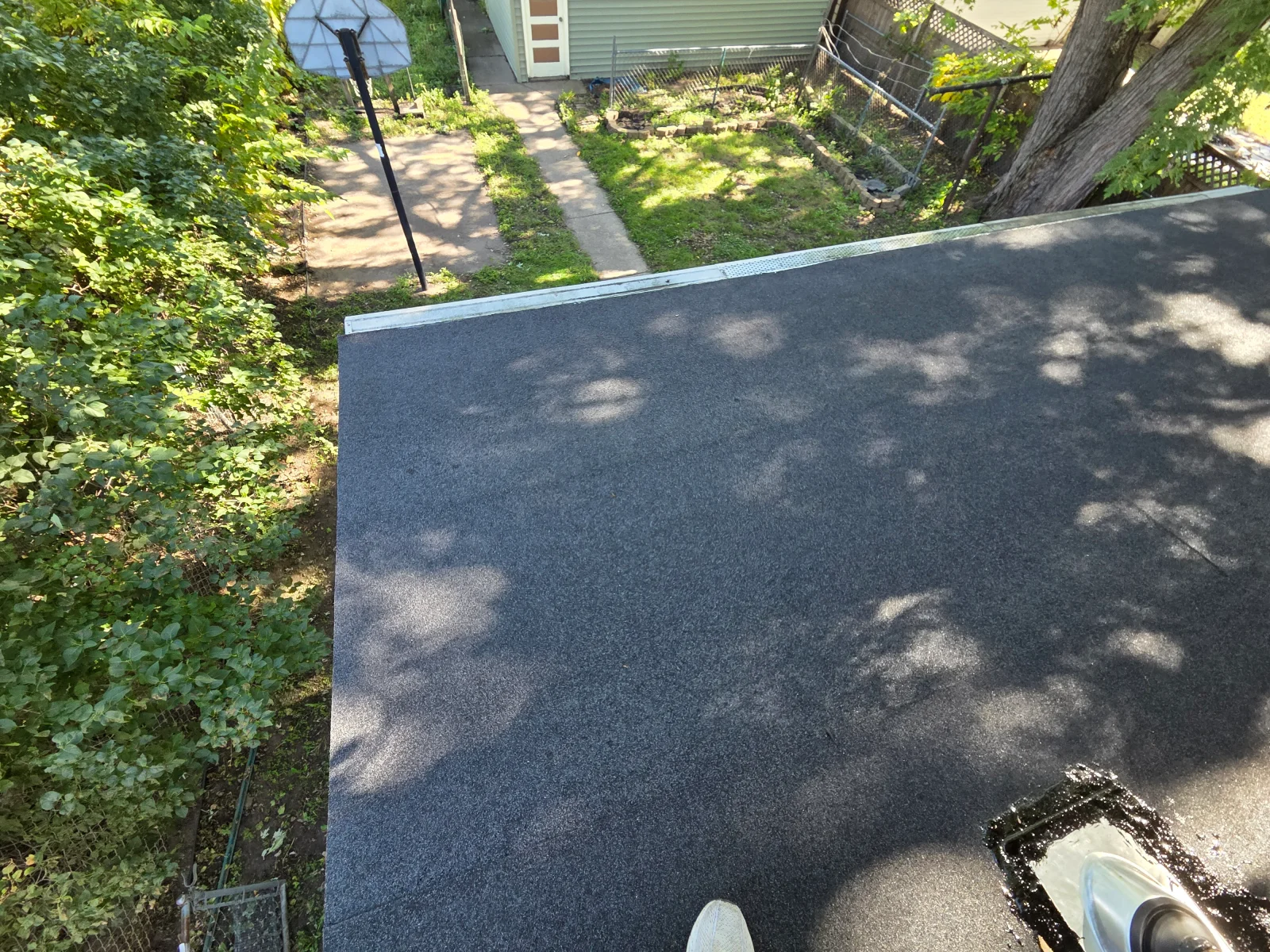Flat roof covered with dark granulated membrane and metal edge flashing, with a sealed roof drain in the foreground